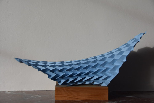 A blue paper sculpture on a wooden stand

Description automatically generated